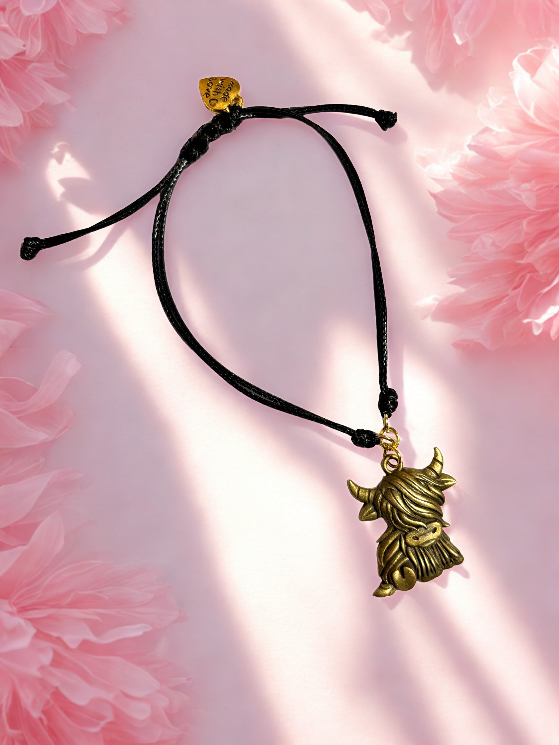 Bracelet with a bronze highland cow charm on a pink floral background