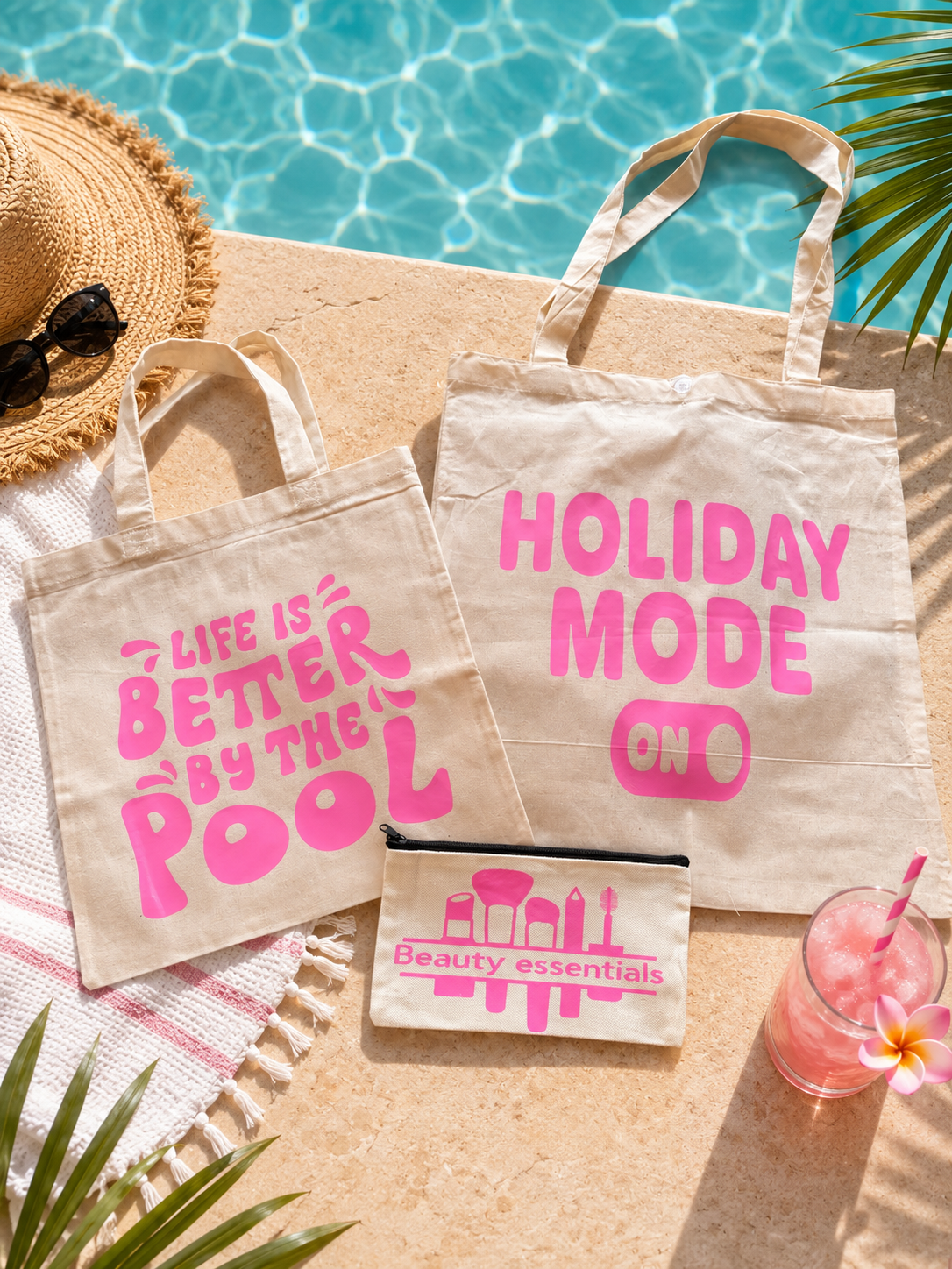 Two tote bags with pink text by a poolside, accompanied by a small pouch and a drink.
