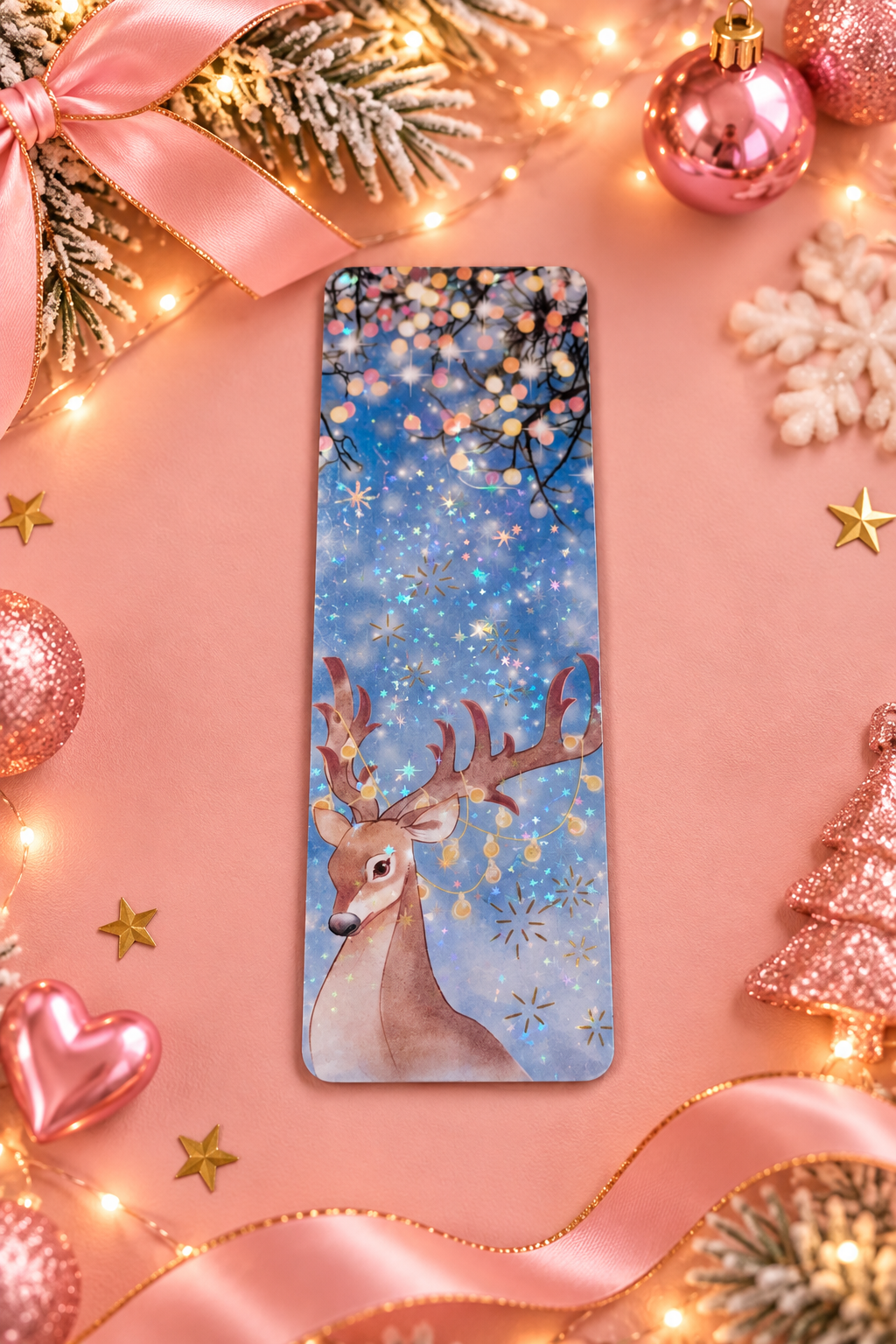 A rectangular bookmark featuring a festive Christmas design with a brown deer, blue snowy background, and colorful lights, styled on a pink background with holiday decorations.