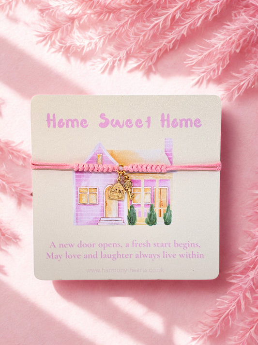 Pink cord bracelet with house and key charms on a card with 'Home Sweet Home' text on a pink background
