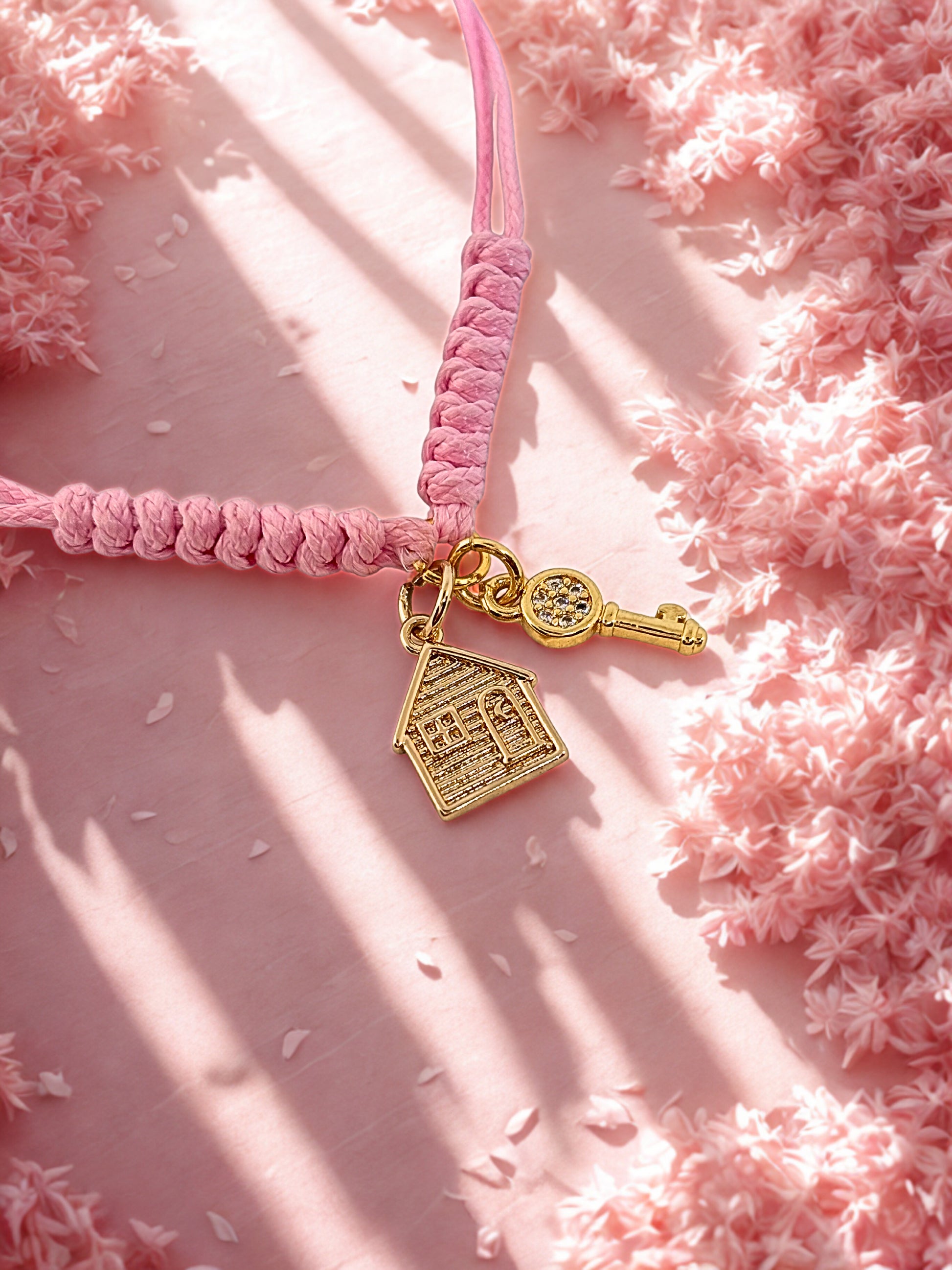 Pink braided cord with gold house and key charm on a pink textured background