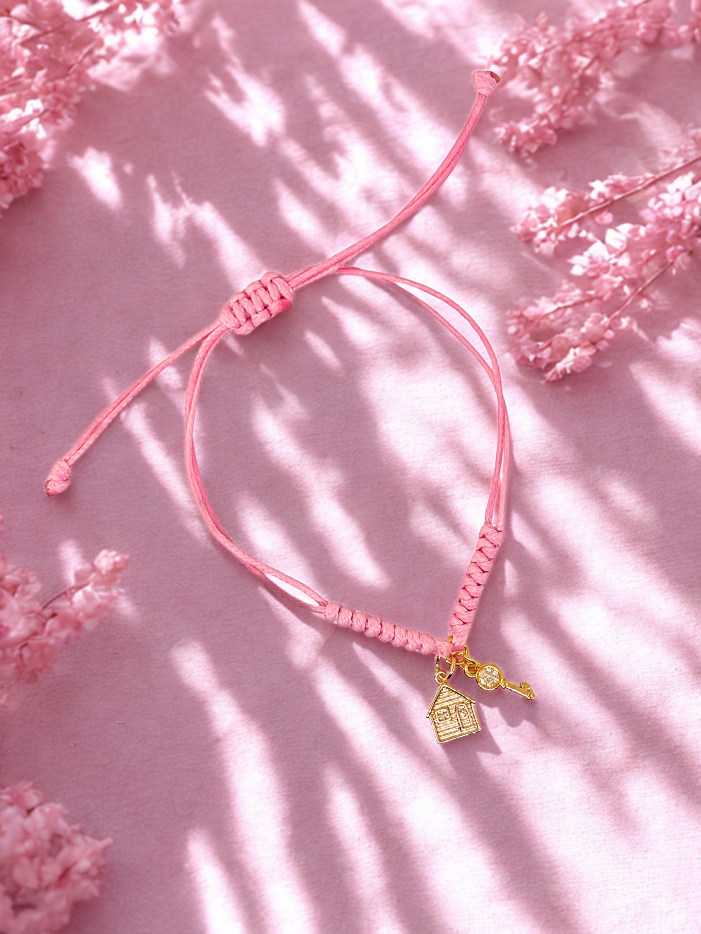 Pink bracelet with a gold house and key charm on a pink floral background