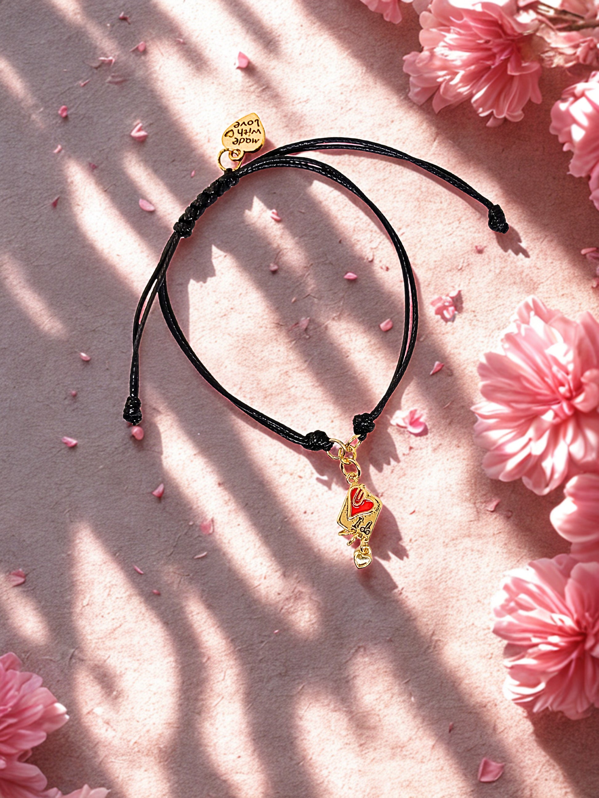 Black cord bracelet with a gold and red charm on a pink floral background