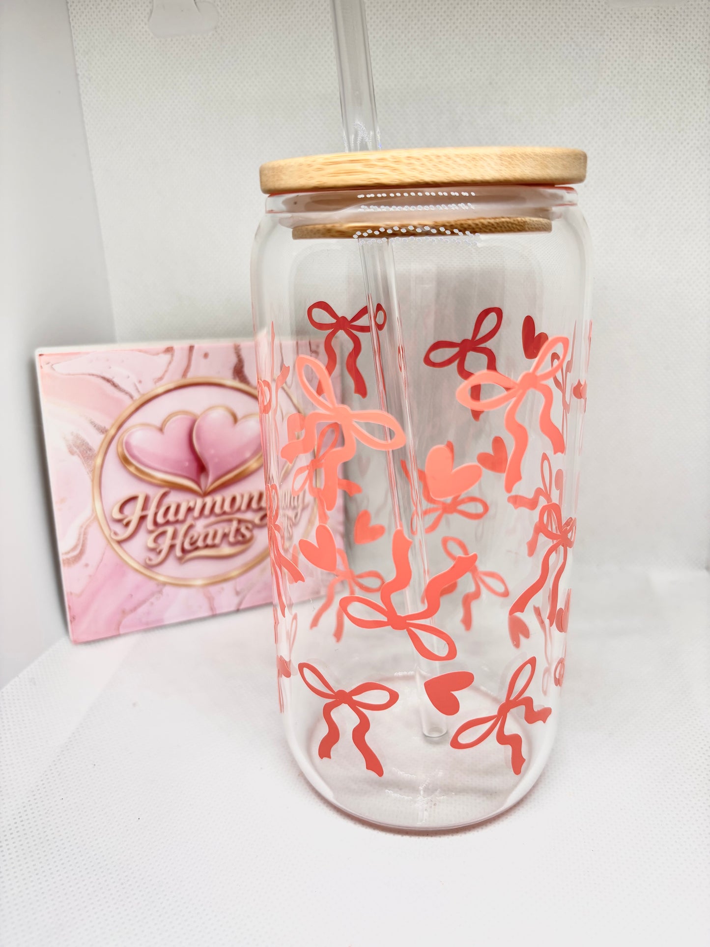 Clear glass with coral bow and hearts designs and wooden lid, next to a pink card with 'Harmony Hearts' logo.