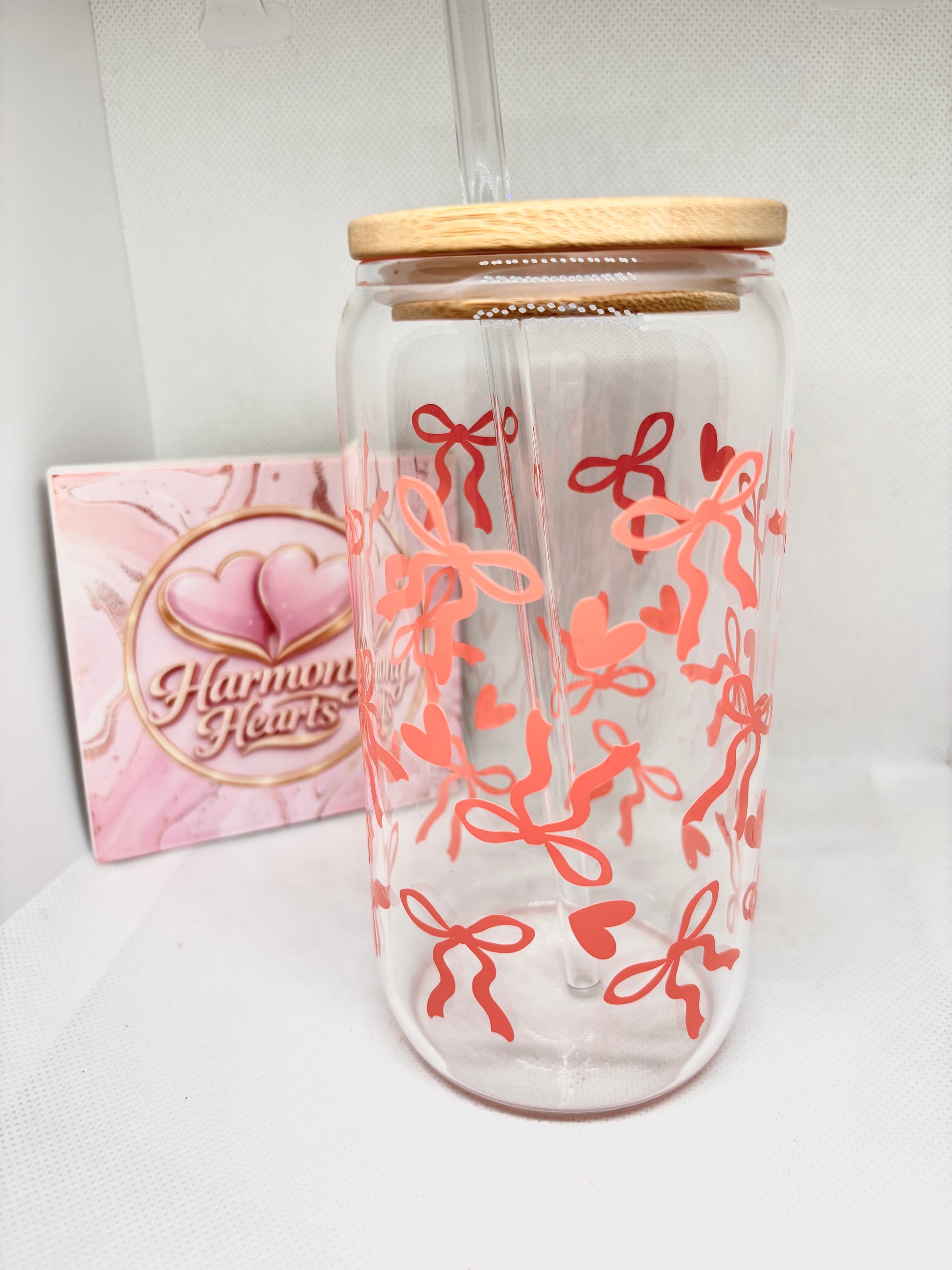 Clear glass with coral bow and hearts designs and wooden lid, next to a pink card with 'Harmony Hearts' logo.