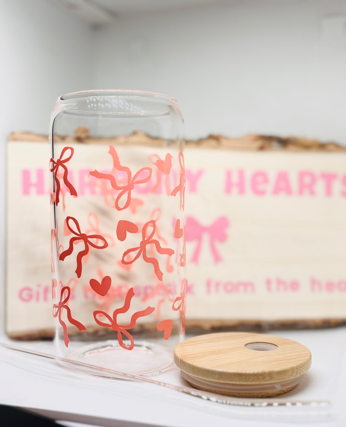 Glass with decorative bows and hearts, wooden lid on a white surface.