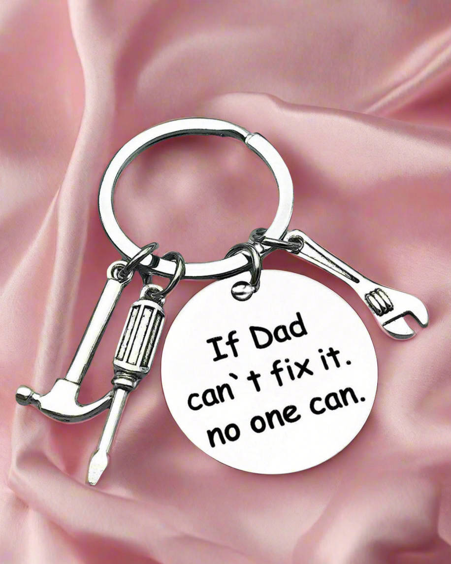 Keychain with tool charms and 'If Dad can't fix it, no one can' quote on a pink fabric background