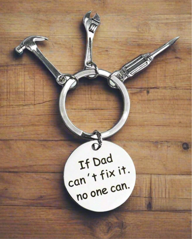 Keychain with tools and 'If Dad can't fix it, no one can' tag on a wooden background