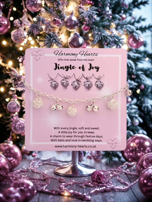 Bracelet with silver bells and balls on a pink card in front of a decorated Christmas tree.