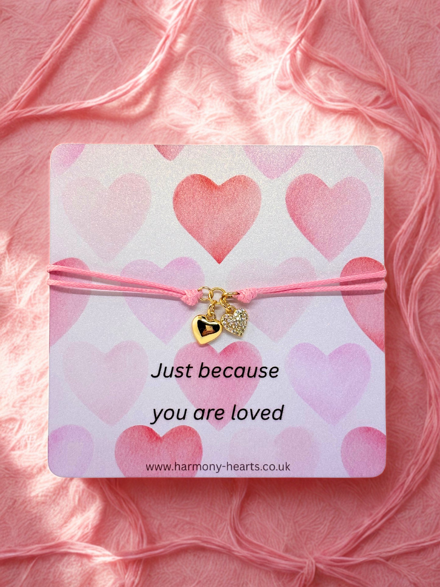 Pink heart-themed bracelet on a card with 'Just because you are loved' text, brand 'Harmony Hearts' visible.