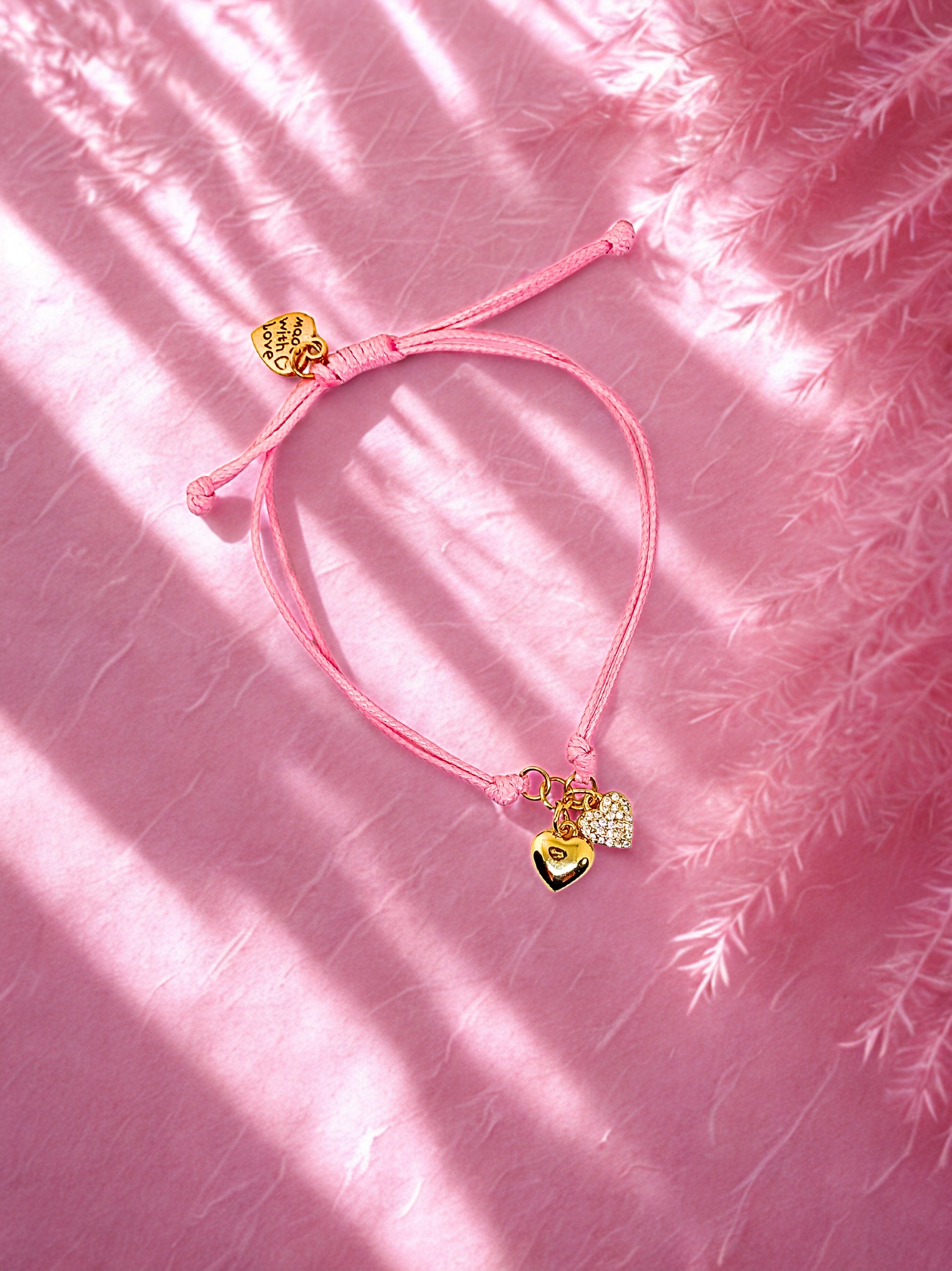 Pink bracelet with heart-shaped charms on a pink textured background