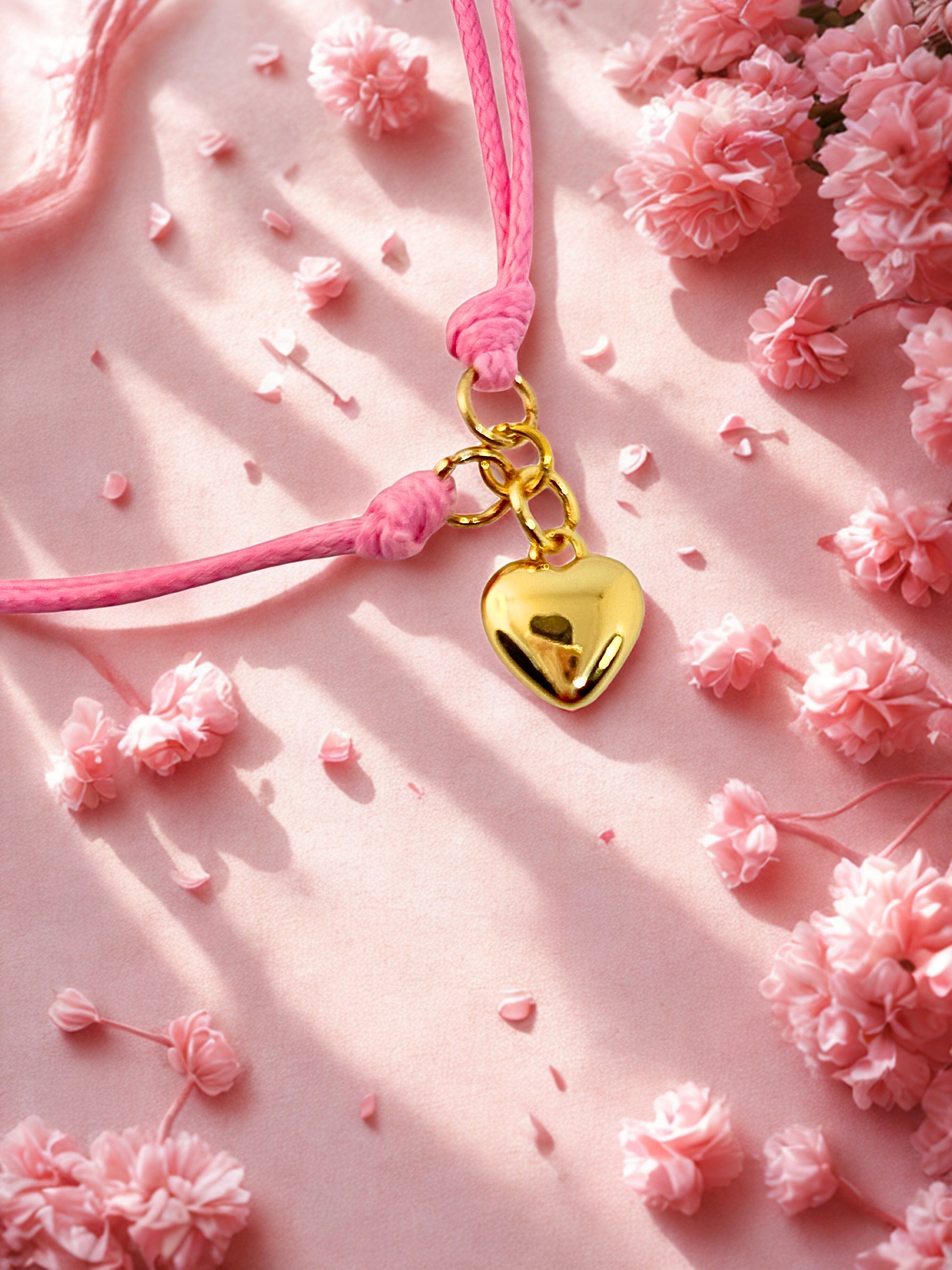 Pink charm bracelet with a gold heart charm on a pink floral background