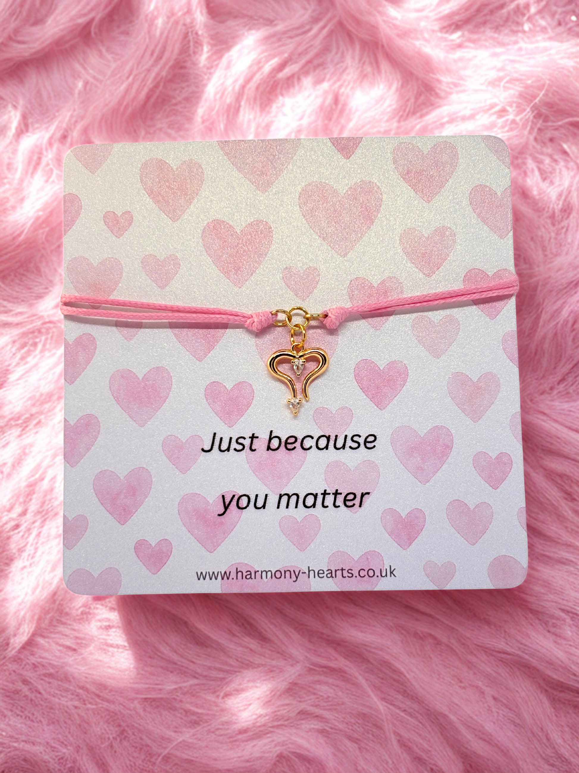 Pink heart-themed bracelet with a gold heart charm on a branded Harmony Hearts card on pink fluffy background