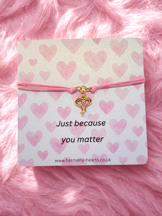 Pink heart-themed bracelet with a gold heart charm on a branded Harmony Hearts card on pink fluffy background