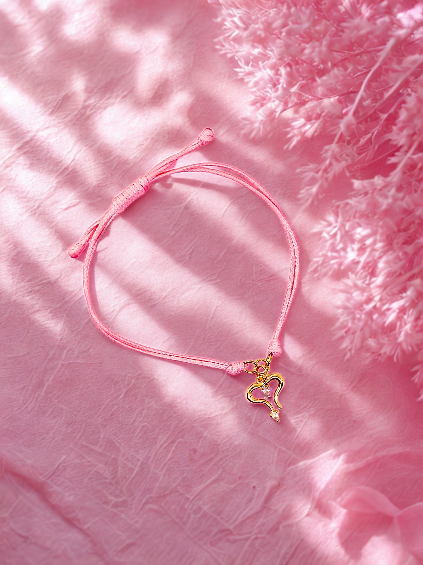 Pink bracelet with a gold heart charm on a pink textured background