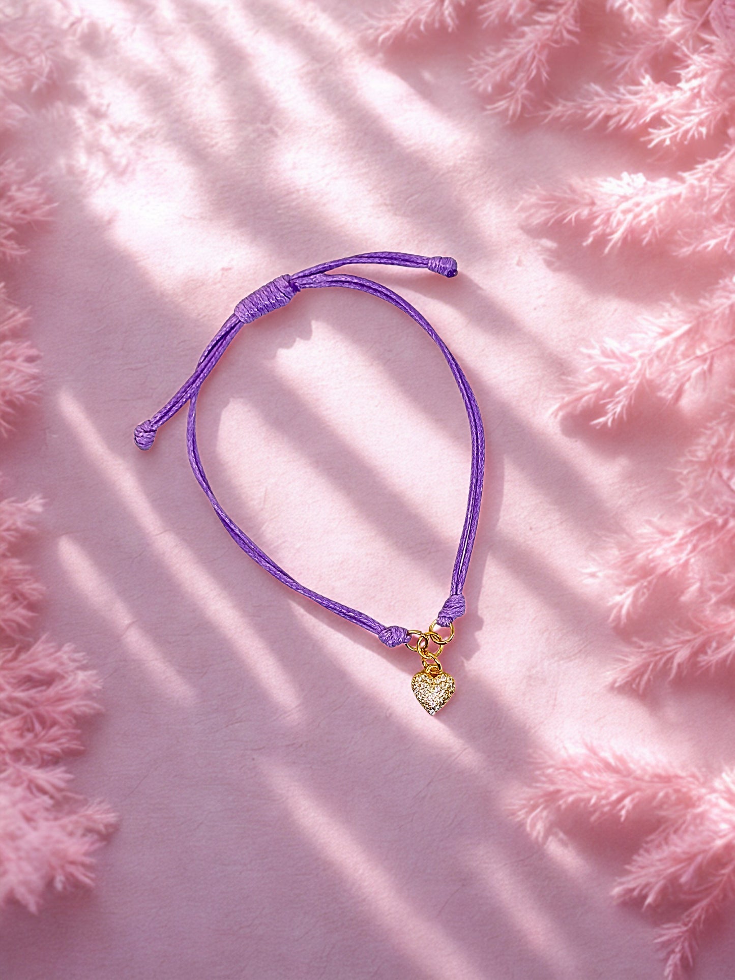 Purple bracelet with a heart-shaped charm on a pink fluffy background