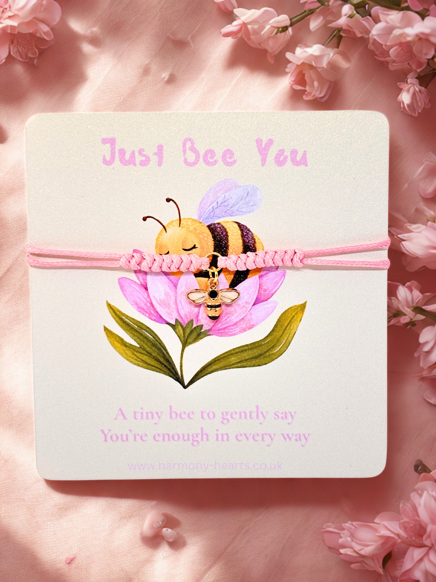 Pink cord bracelet with bee charm on a branded Harmony Hearts card with a bee and flower illustration and 'Just Bee You' text on a pink floral background.
