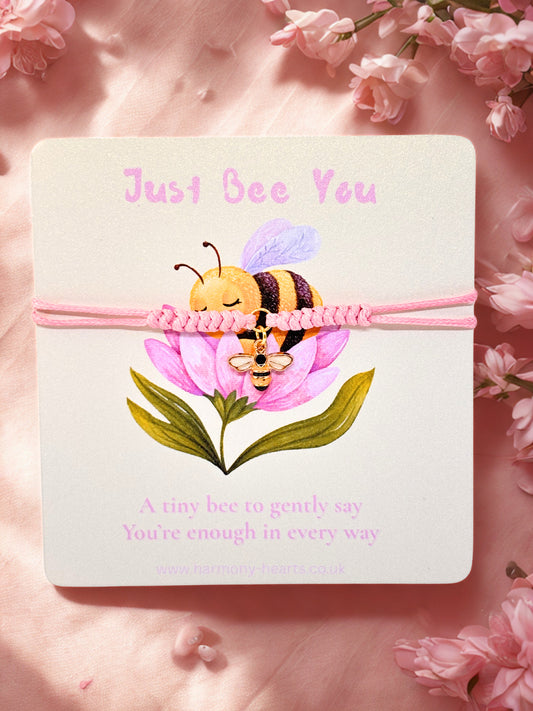 Pink cord bracelet with bee charm on a branded Harmony Hearts card with a bee and flower illustration and 'Just Bee You' text on a pink floral background.