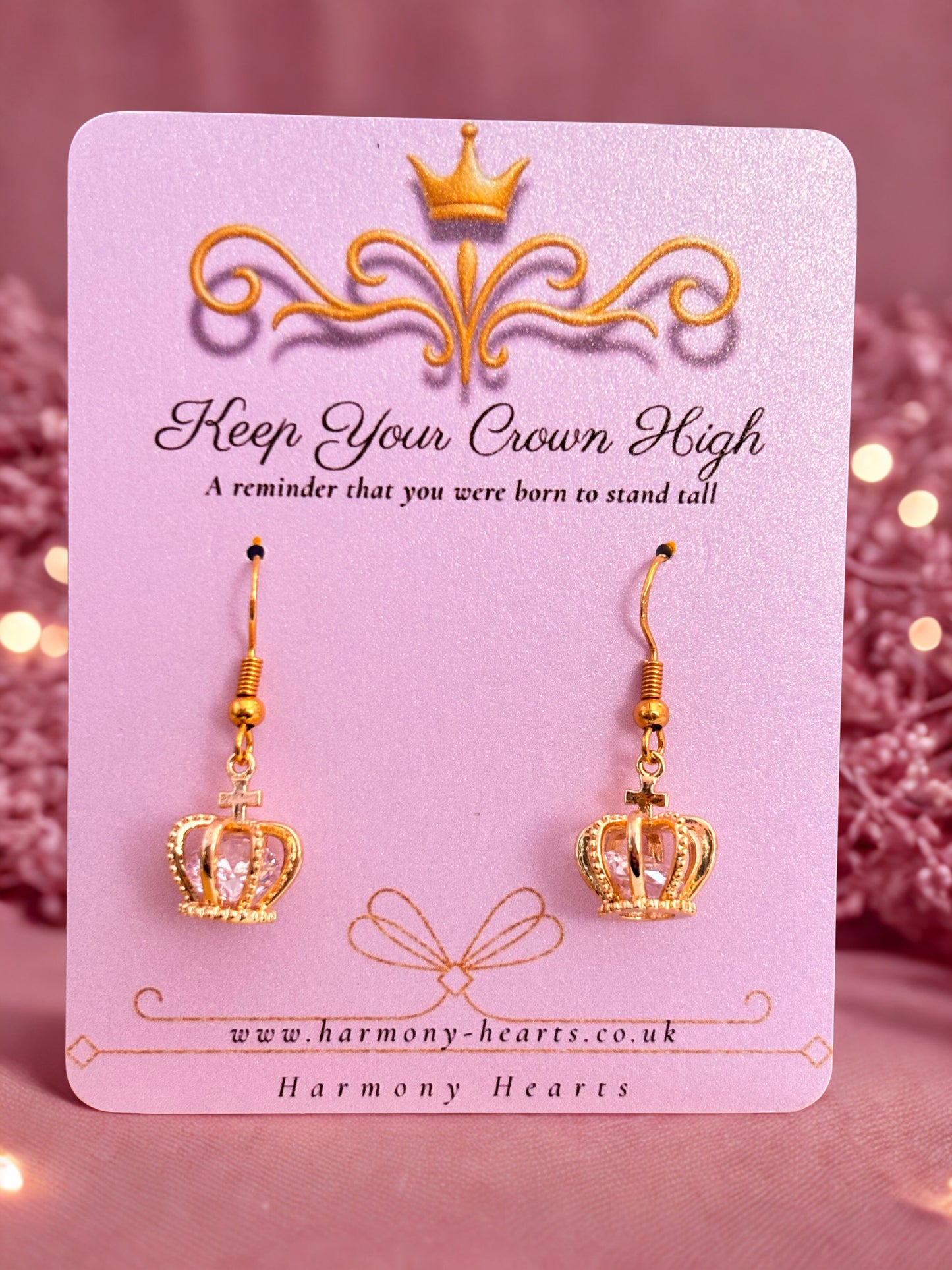 Gold crown earrings on a pink card with decorative elements and text.