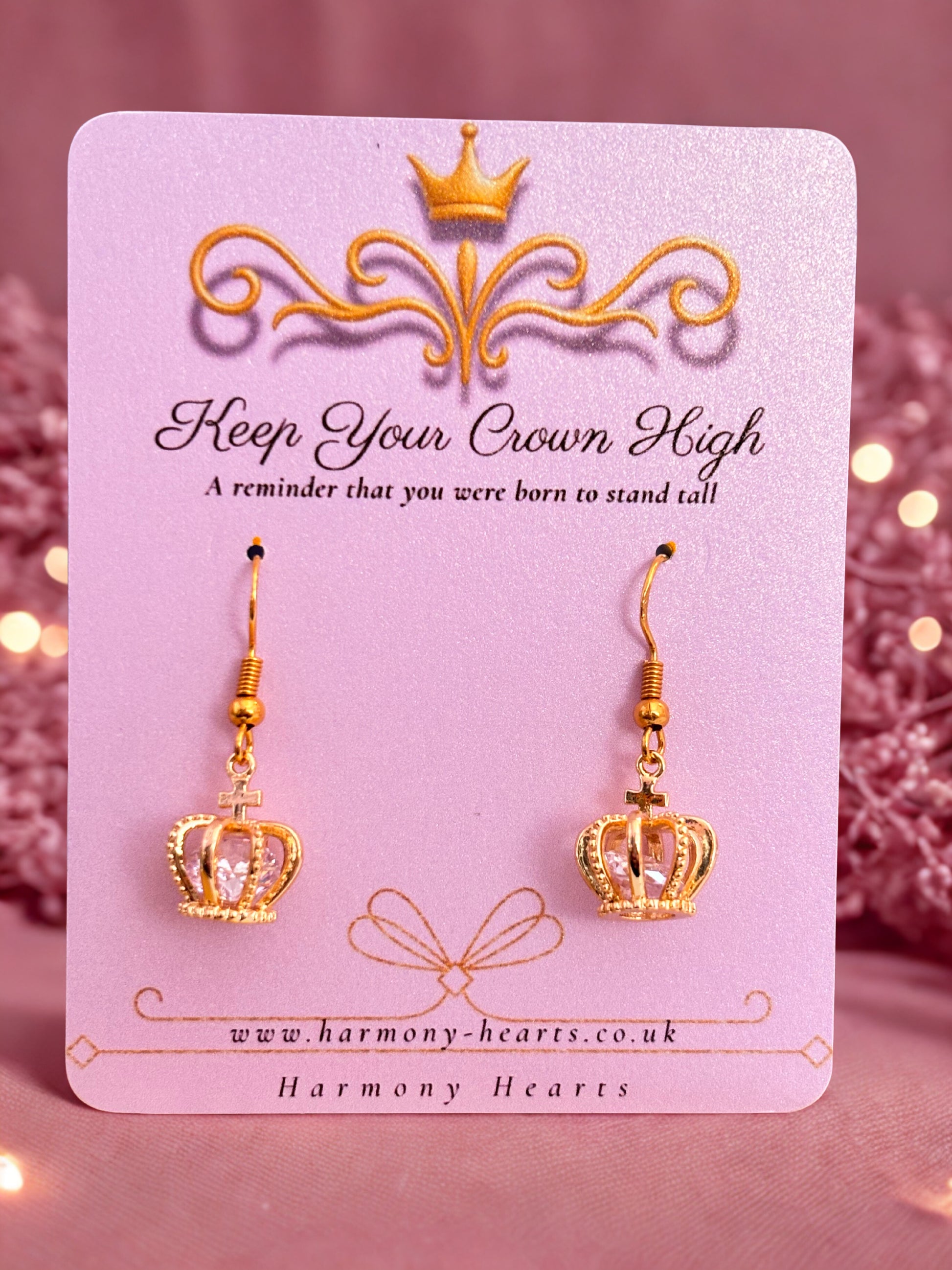Gold crown earrings on a pink card with decorative elements and text.