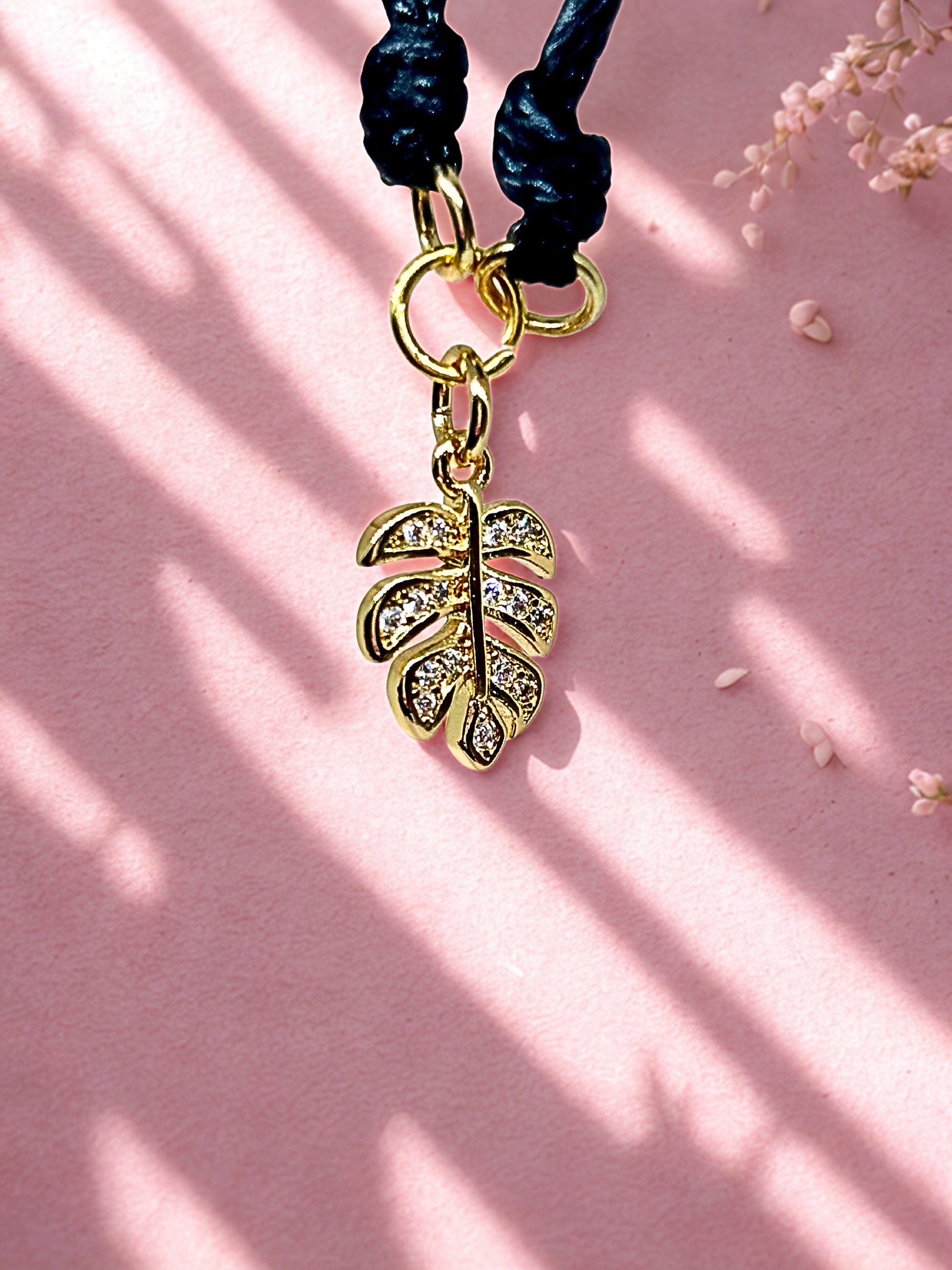 Gold leaf charm on a black cord against a pink background