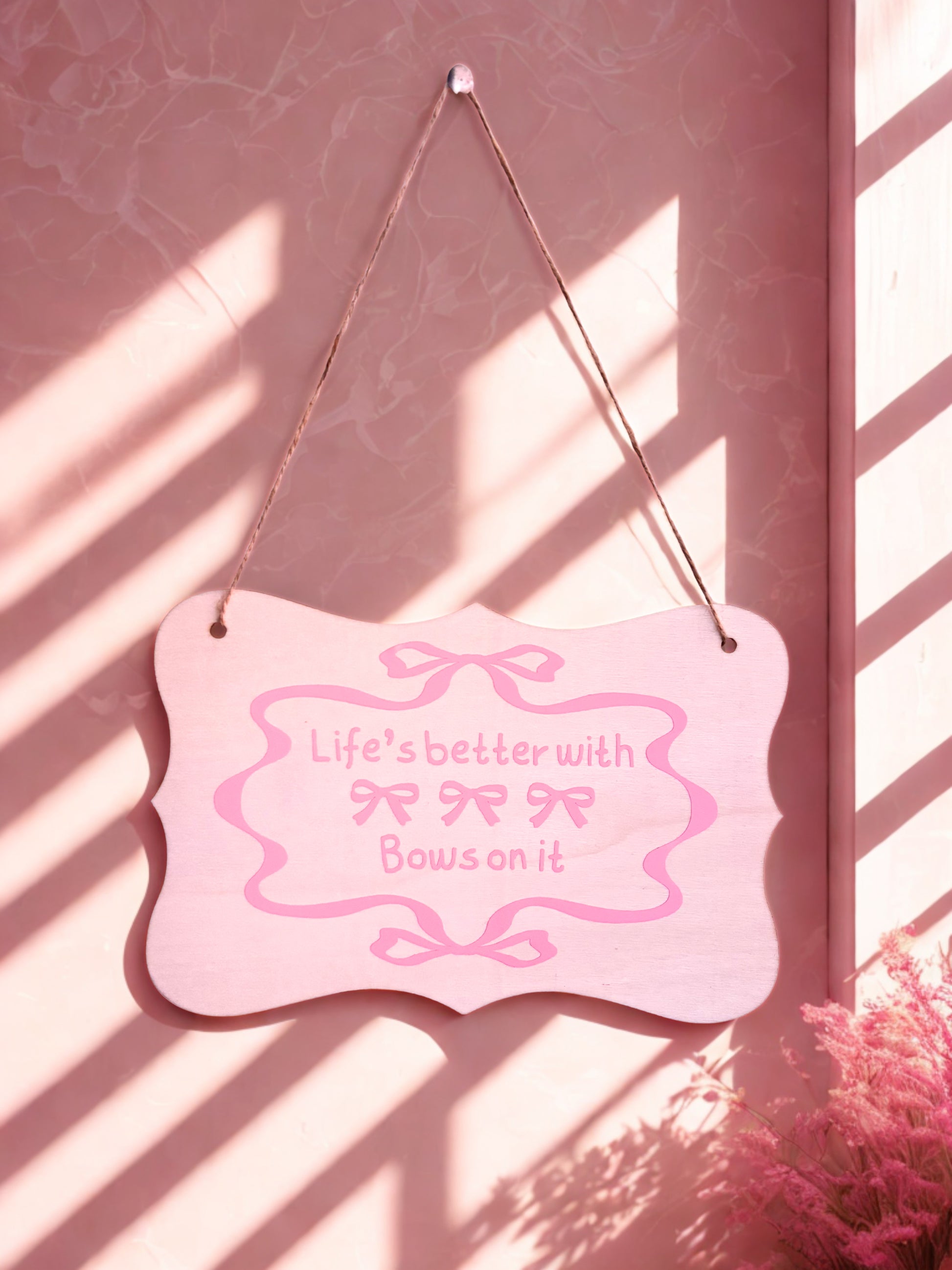 Pink sign with 'Life's better with bows on it' text hanging against a pink wall.