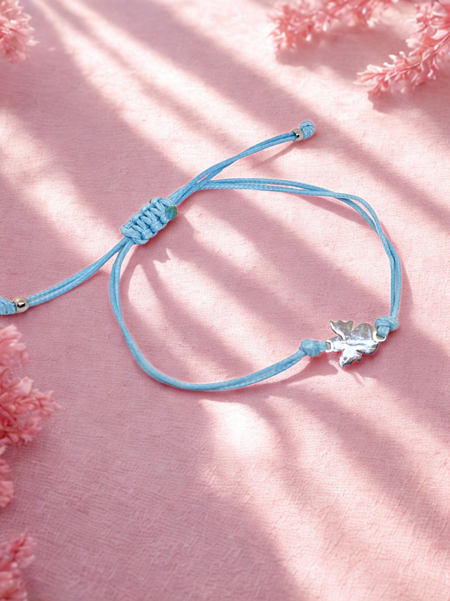 Blue bracelet with a silver angel charm on a pink fabric background