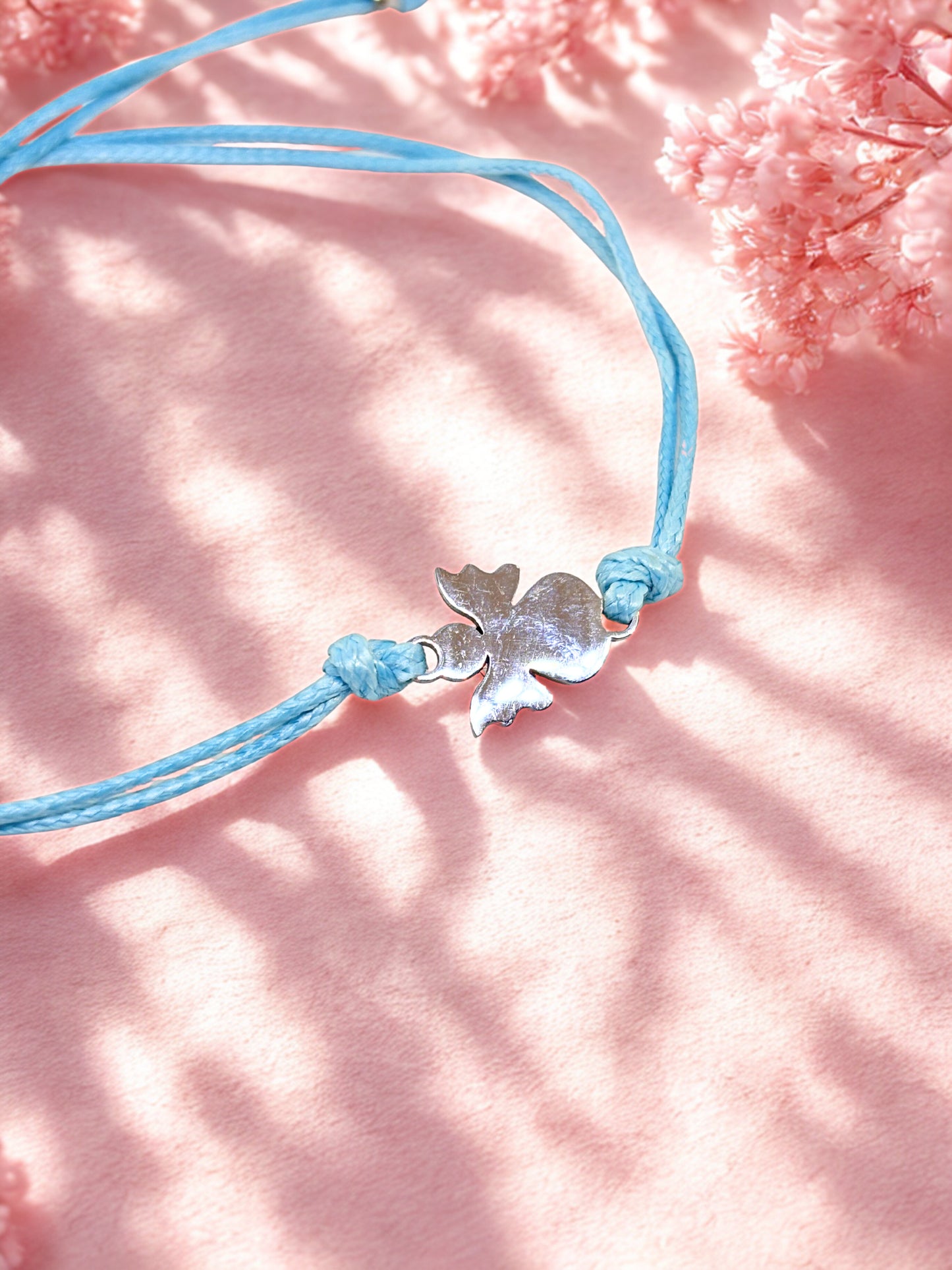 Blue cord bracelet with a silver angel charm on a pink textured background