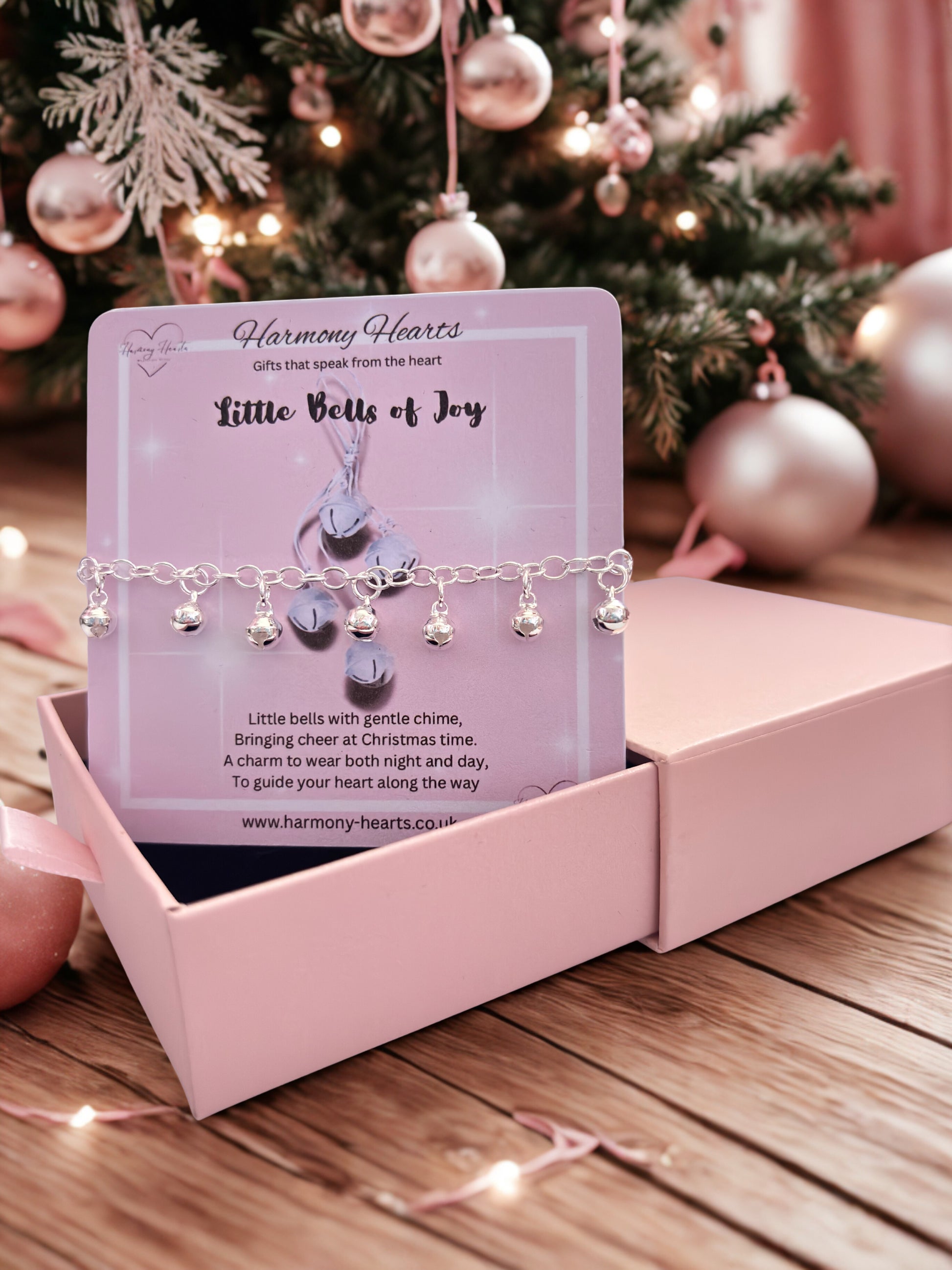 Bracelet with bells on a Harmony Hearts card in front of a decorated Christmas tree.