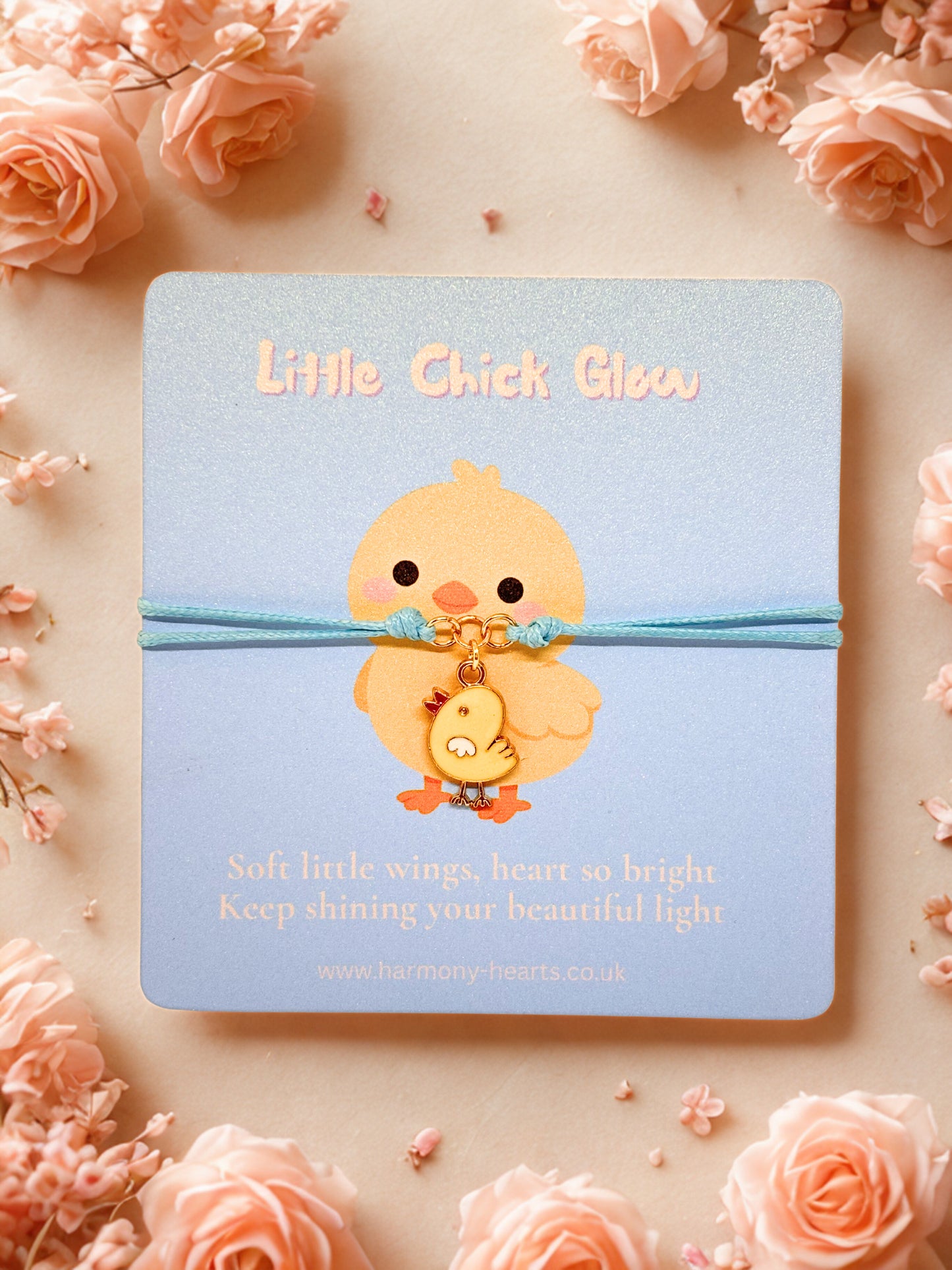 Blue cord bracelet with a chick charm on a branded Harmony Hearts card with a chick charm on a blue background surrounded by pink flowers