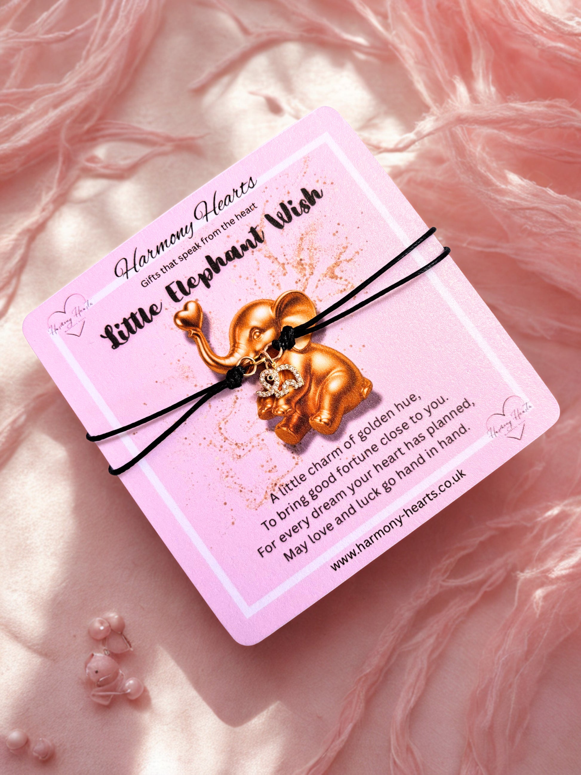 Gold elephant charm bracelet on a pink card with text, against a soft pink background