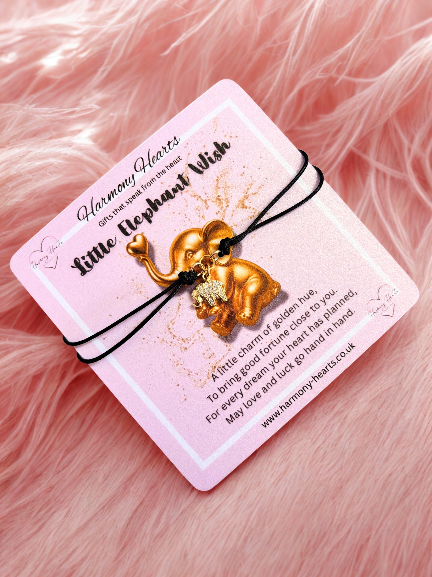 Gold elephant charm bracelet on a pink card with text, against a pink fluffy background