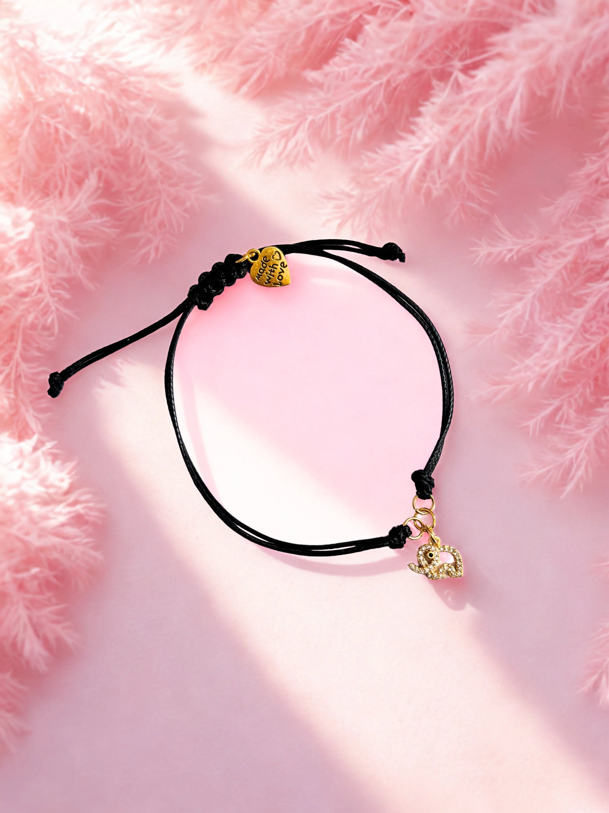 Black cord bracelet with gold elephant charms on a pink fluffy background