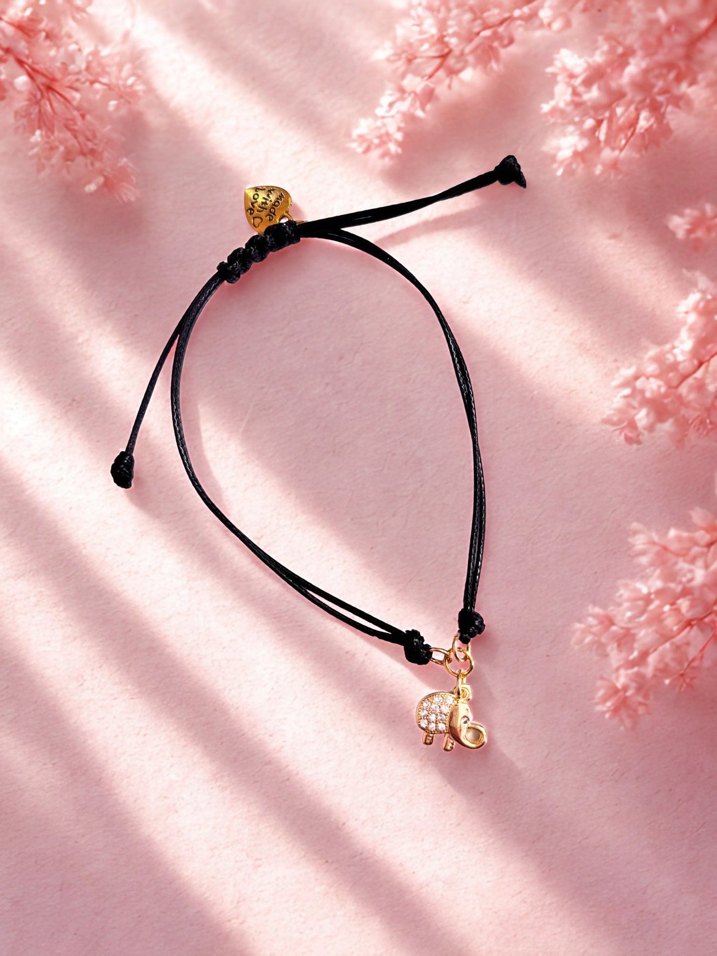 Black cord bracelet with gold elephant charm on a pink floral background