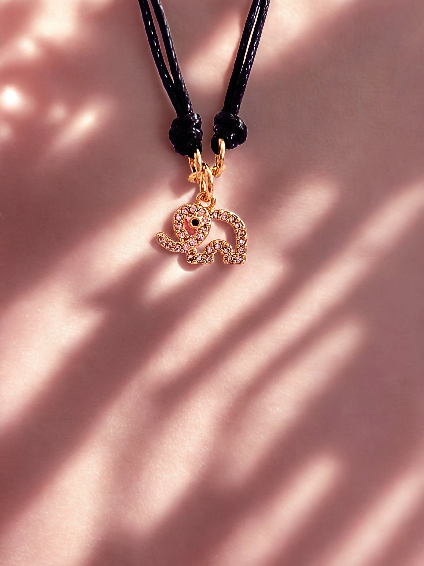 Bracelet with a gold elephant charm on a pink background