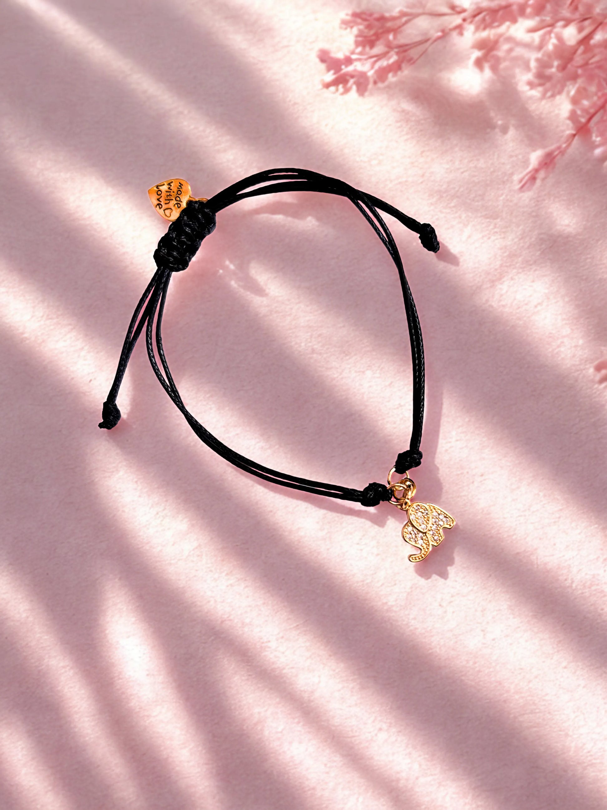 Black cord bracelet with gold elephant charms on a pink background
