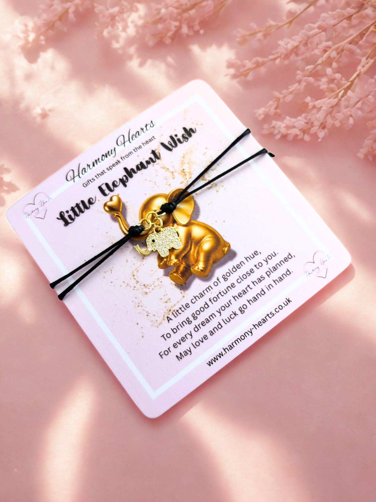 Gold elephant charm on a black cord with a card on a pink background