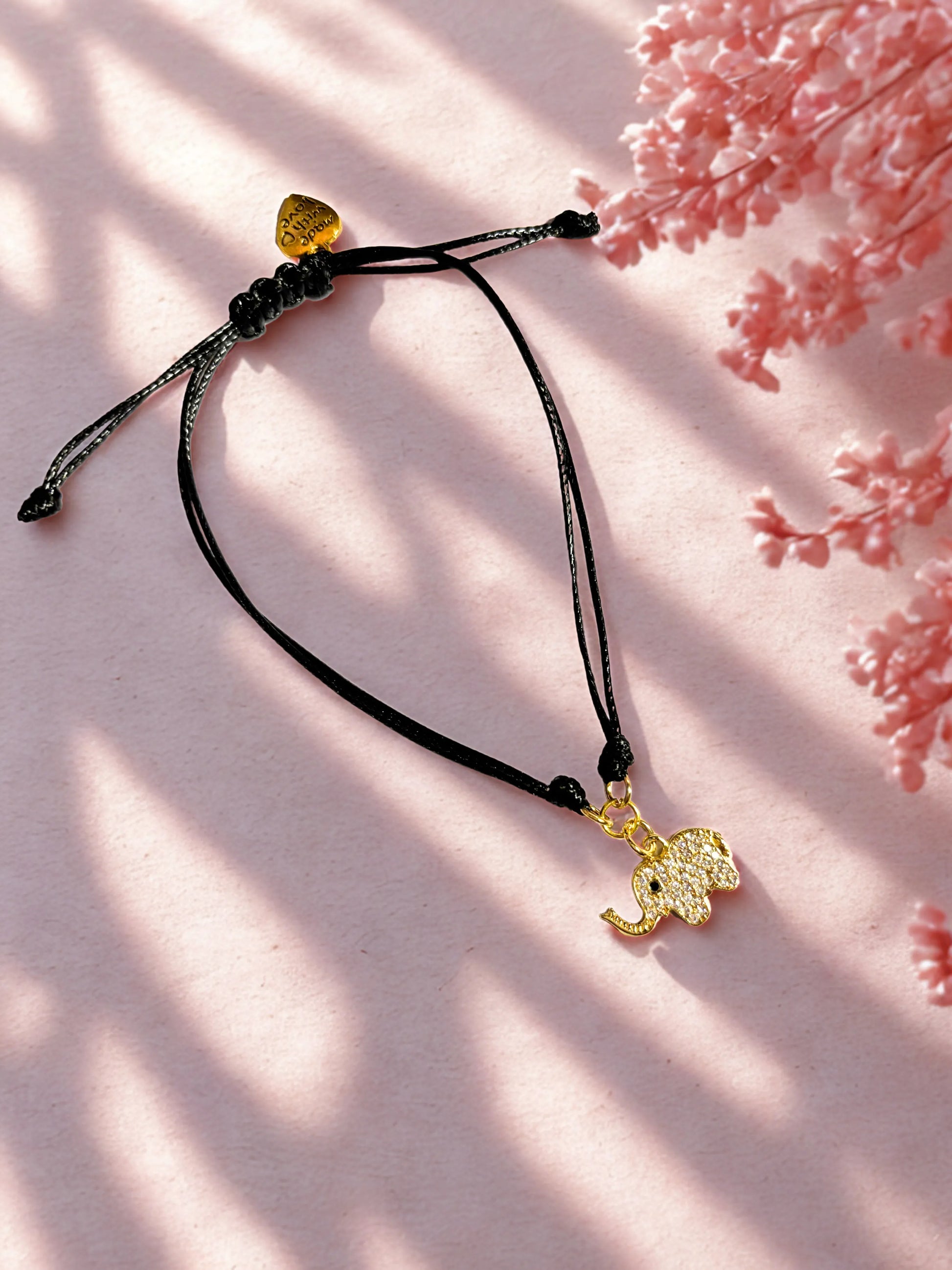 Black cord with a gold elephant pendant on a pink floral background