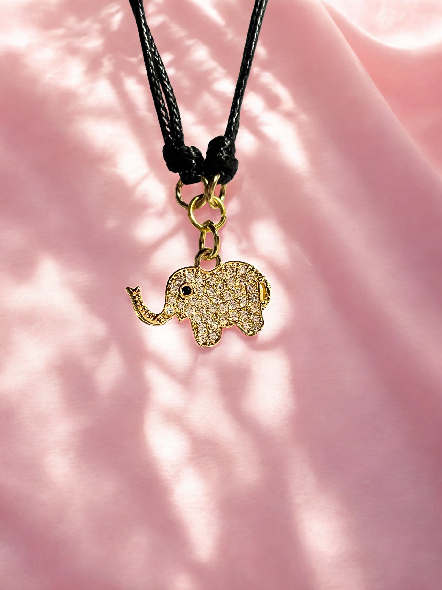 Gold elephant pendant on a black cord against a pink fabric background