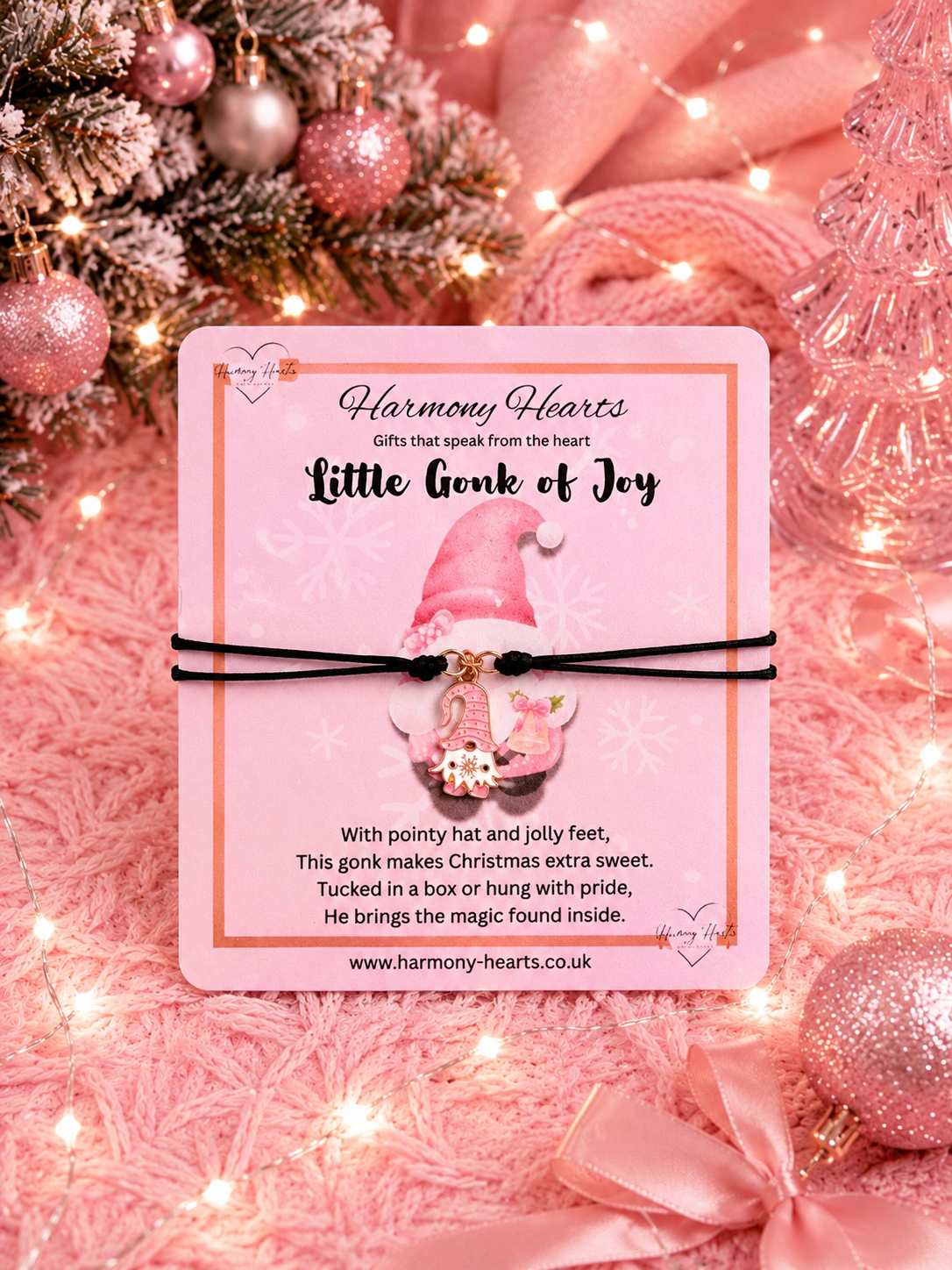 Festive pink card with Harmony Hearts branding with a black cord charm bracelet and a pink gonk charm