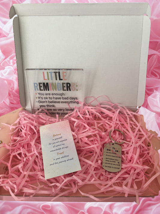 Gift box with pink interior, containing a bottle labeled 'Little Reminder' and a keychain with a tag.