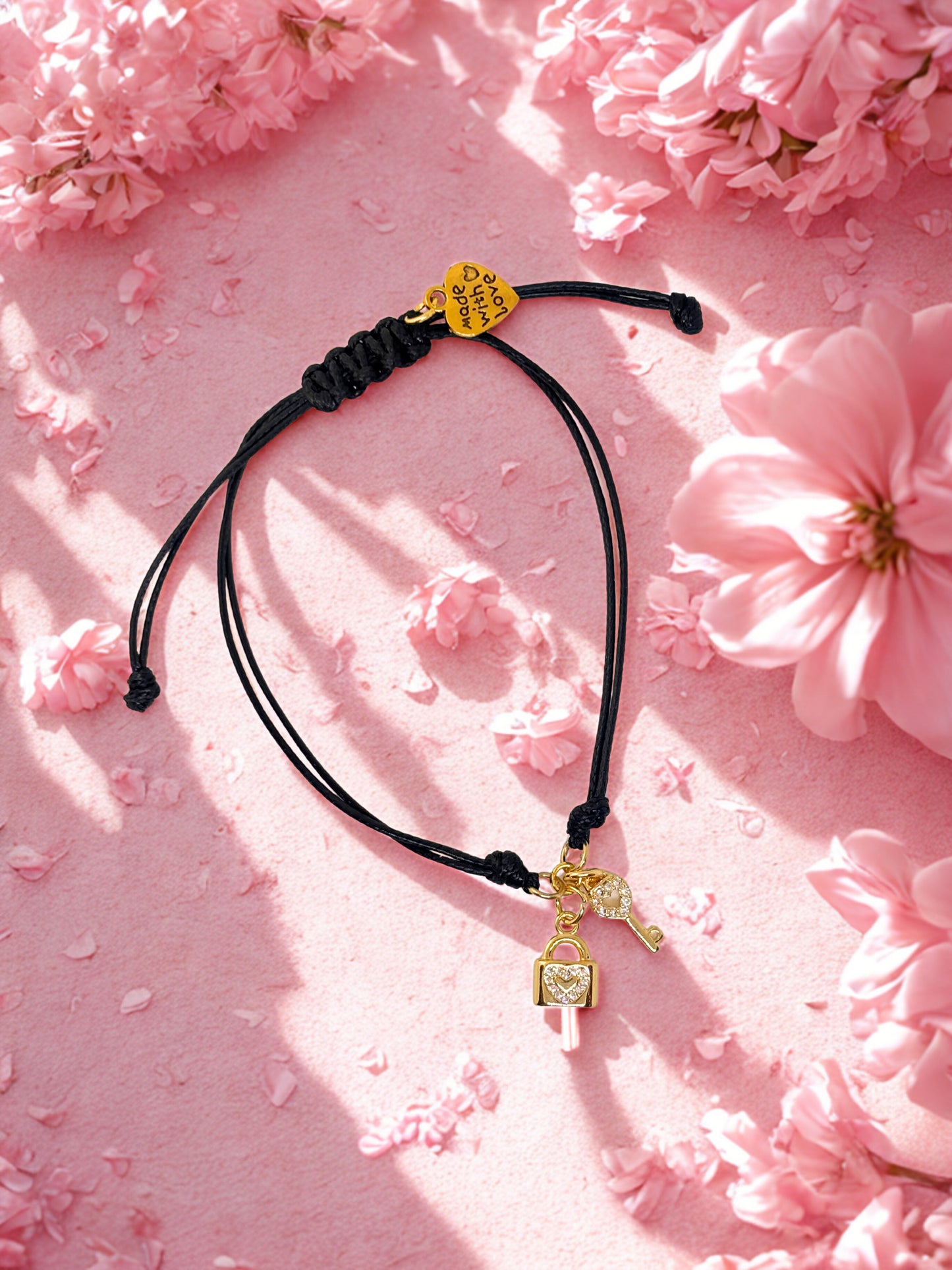 Black cord bracelet with gold key and lock charms on a pink floral background