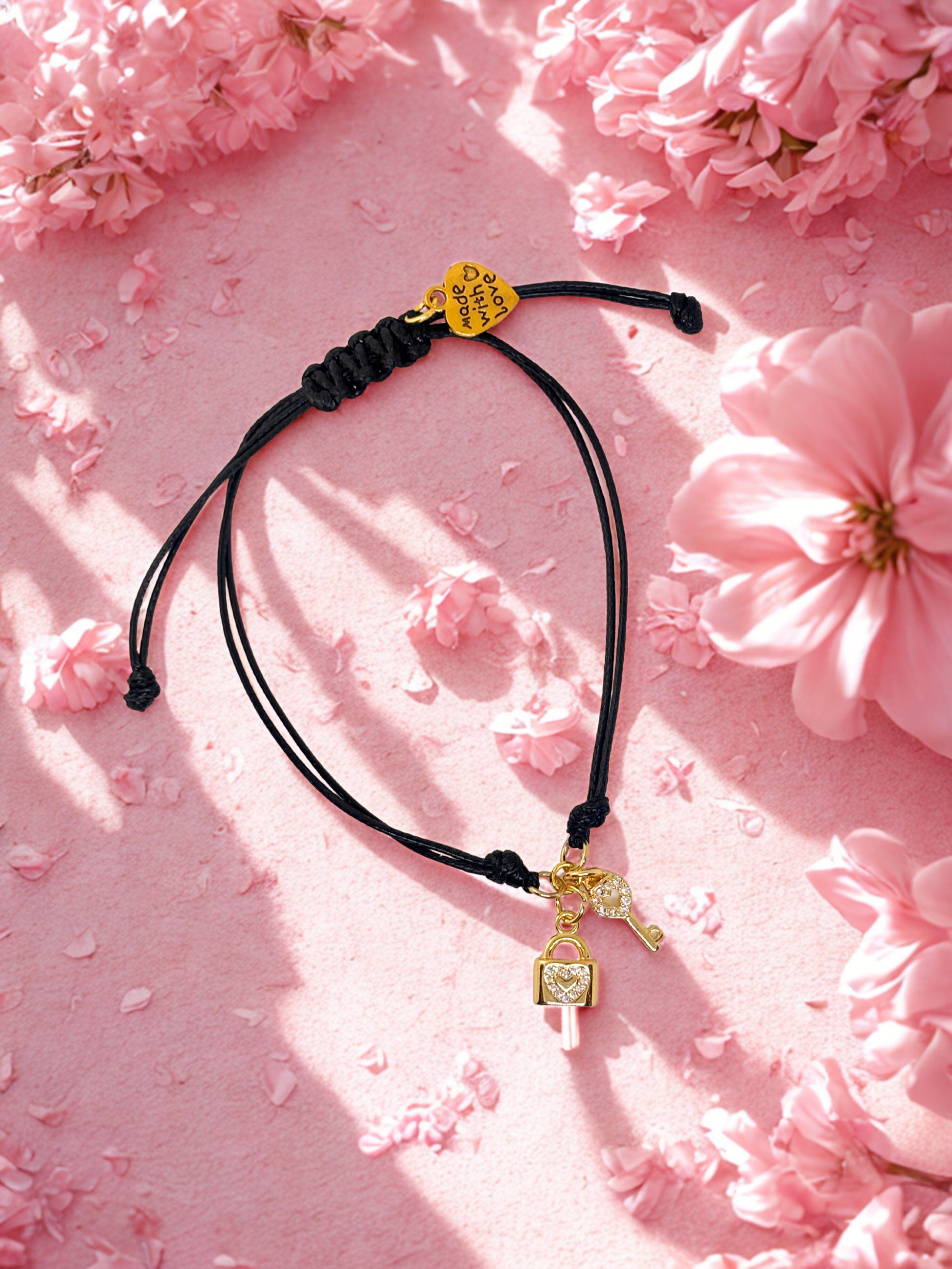 Black cord bracelet with gold key and lock charms on a pink floral background
