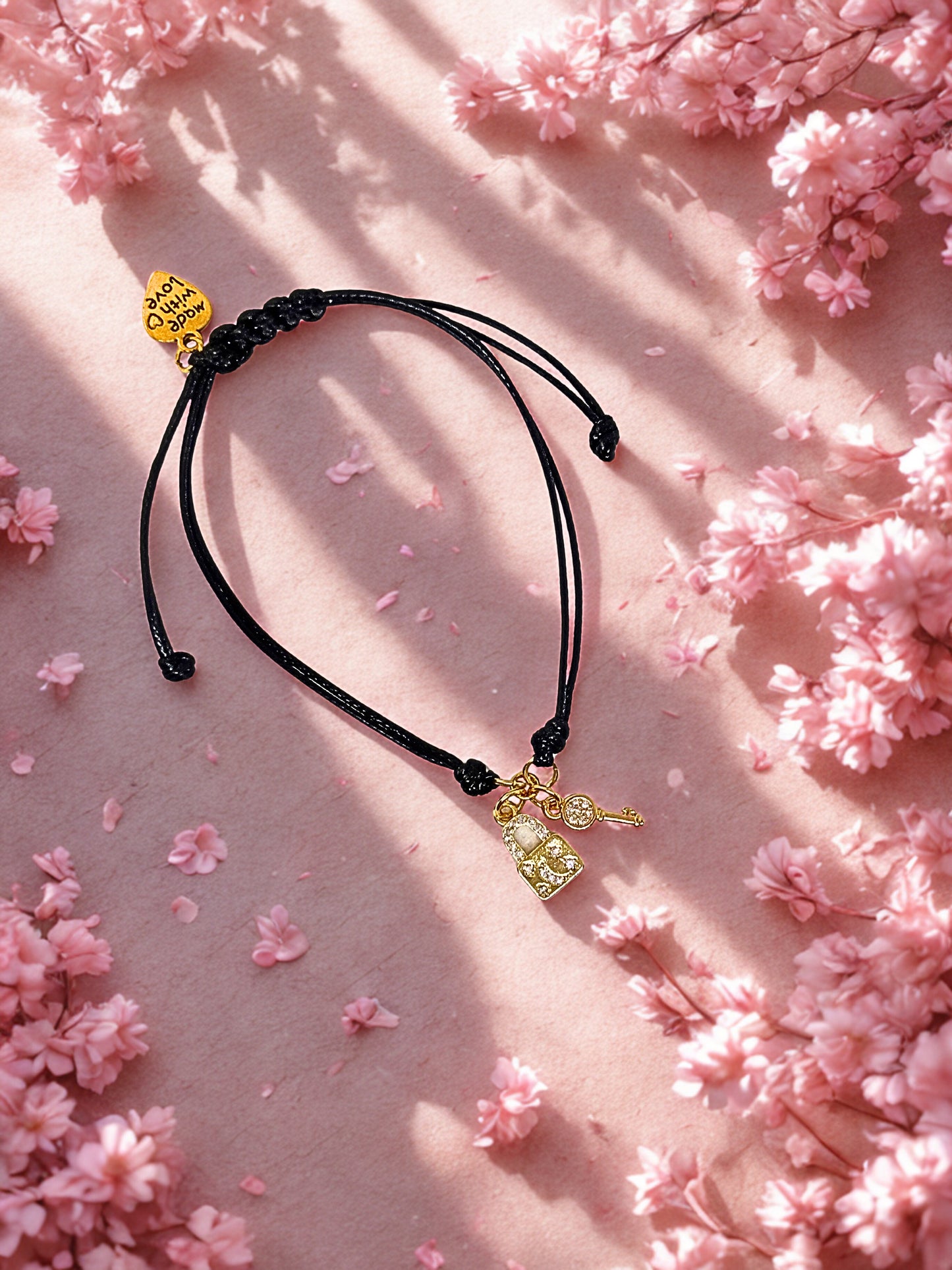 Black cord bracelet with gold key and lock charms on a pink floral background