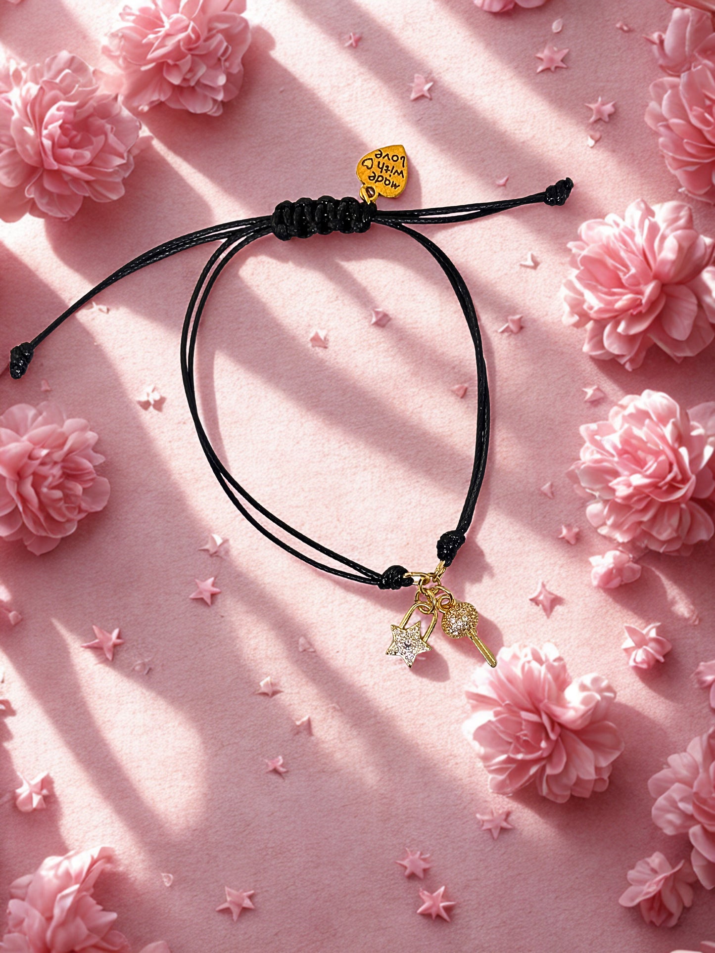 Black cord bracelet with a gold and crystal key and lock charms on a pink floral background