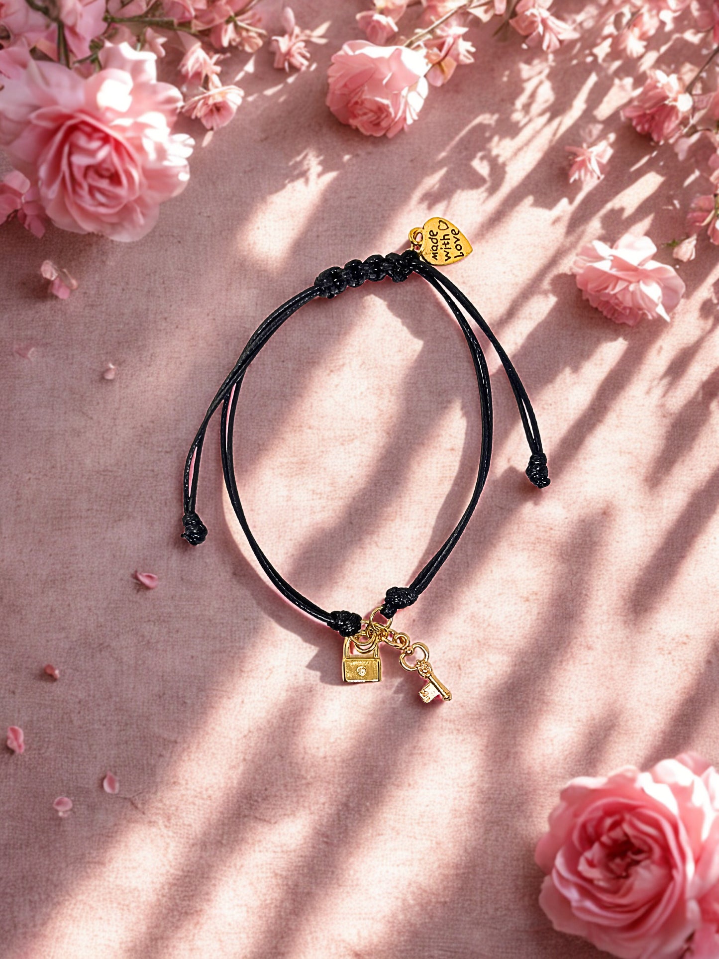 Black cord bracelet with gold lock and key charms on a pink floral background