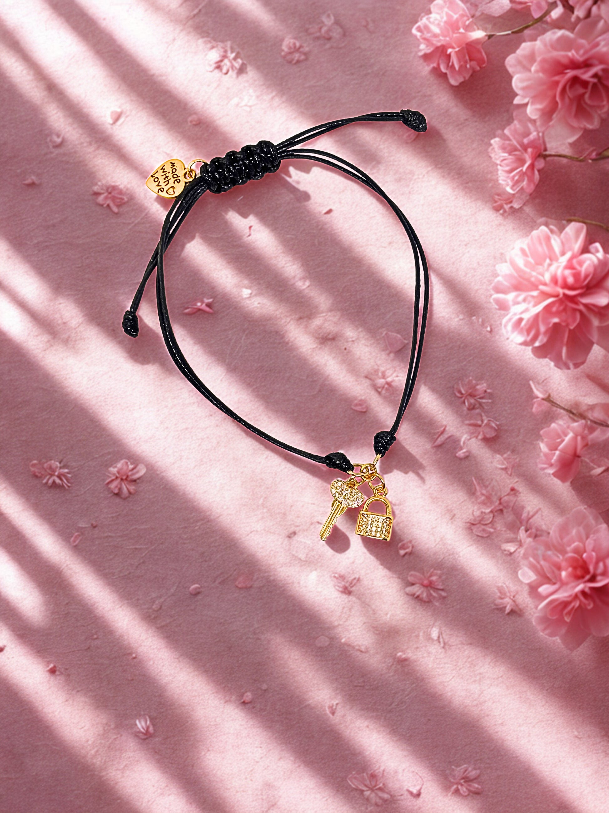 Black cord bracelet with gold lock and key charms on a pink floral background