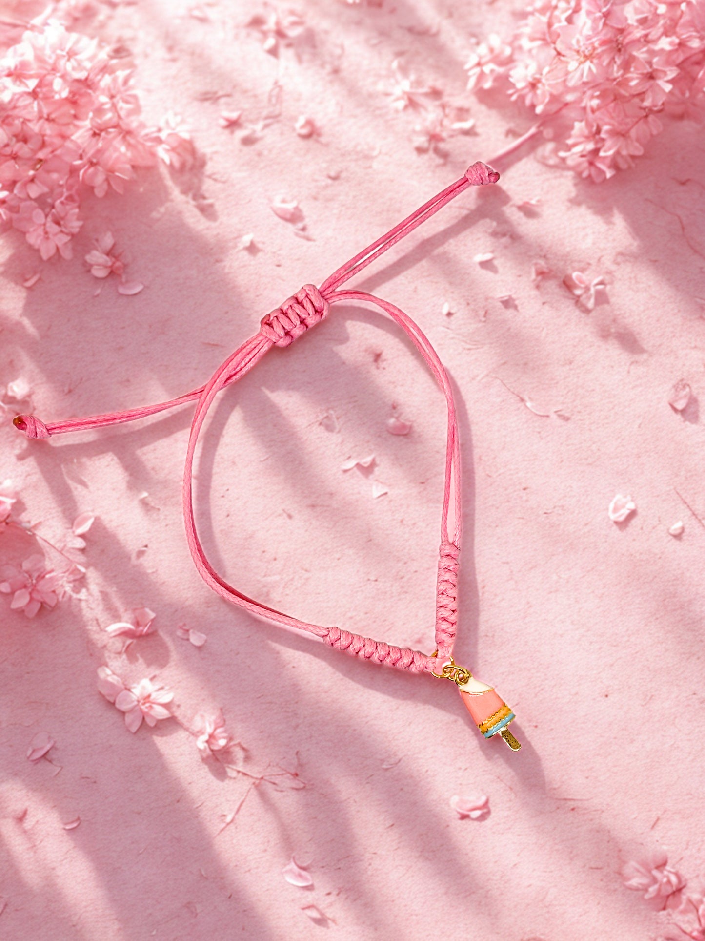 Pink braided bracelet with a colourful lolly charm on a pink floral background
