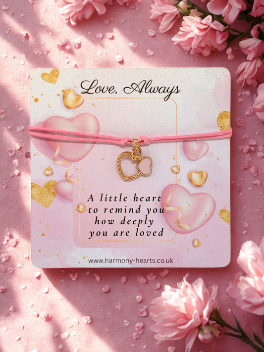 Pink bracelet with heart charm on a pink card with 'Love, Always' text, surrounded by pink flowers.