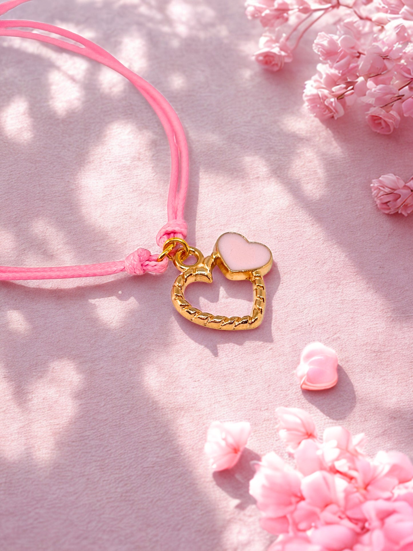 Pink cord bracelet with a gold heart-shaped charm on a pink floral background
